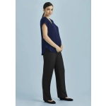 A woman wearing a navy top and black maternity pants stands against a light blue background, smiling and holding her belly.