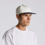 A cap featuring a two-tone design with a light-coloured crown and a navy peak, worn by a model.