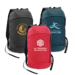Three compact backpacks in grey, teal, and red, each featuring a logo on the front.