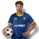A blue men's soccer jersey with yellow accents and a logo, held by a man with a soccer ball.