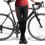 Custom women's cycling pants in black with red side stripes, paired with a bicycle. Features a branding logo.