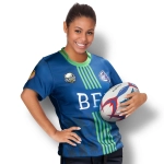 A woman wearing a blue and green custom women's rugby t-shirt, holding a rugby ball and smiling. The shirt features a logo.