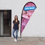 A small tear drop flag kit featuring a vibrant design, with a woman standing beside it, showcasing its height and structure.