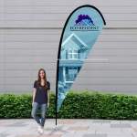 A medium teardrop flag kit featuring a logo, with a blue and white design, alongside a standing woman outdoors.