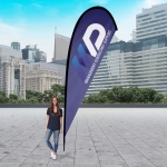A large teardrop flag kit in blue, featuring a logo, displayed outdoors with a city skyline in the background.