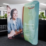 A small curved stretch media wall in green and white featuring images of people and branding elements.