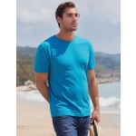 A blue t-shirt worn by a man standing on a beach, with mountains in the background and a straw hat in his hands.