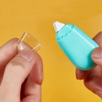 A turquoise glue tape dispenser with a clear cap held in hands, set against a yellow background.