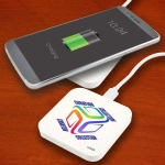 A square wireless charger in white with a logo, placed beneath a smartphone displaying a charging battery icon.