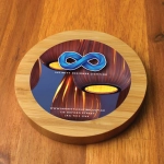 A round bamboo wireless charger with a colorful design featuring a logo, placed on a wooden surface.