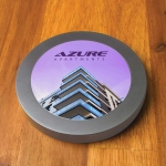A round, metallic wireless charger with a colorful graphic featuring a modern apartment building.