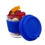 A glass coffee cup with a blue silicone sleeve, filled with assorted jelly lollies in various colours.