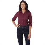 A burgundy long sleeve button-up shirt for women, featuring a logo on the sleeve, paired with dark jeans.