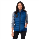A woman wears a blue insulated vest over a grey long-sleeve top, smiling and posing for the image.