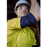 A rugged long sleeve shirt in yellow and navy, featuring reflective elements and a logo, worn by a person in safety gear.