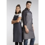 Two models wear Urban Bib Aprons in dark grey and charcoal, featuring pockets and a logo.