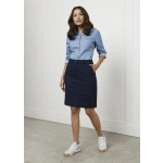 A woman in a fitted navy skirt, paired with a light blue shirt and white sneakers, standing against a white wall.