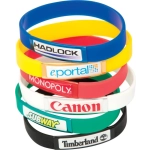 A stack of silicone wristbands in various colours, featuring different logos and branding on each band.