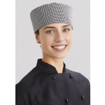 A chef cap in a black and white checkered pattern, worn by a smiling individual in a black chef's uniform.