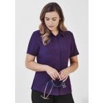 A plain short sleeve shirt in purple, featuring a button-up design and a chest pocket, held by a woman with a stethoscope.