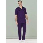 A man wears purple scrub pants with a matching scrub top and stethoscope, set against a pale background.