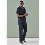 A man is wearing navy unisex scrub pants and a matching scrub top, standing against a plain green background.