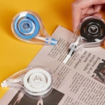 Three correction tape dispensers in blue, white, and black, placed on a magazine against a yellow background.