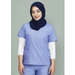 A woman wearing a light blue scrub top with two pockets, layered over a white long-sleeve shirt, and a navy hijab.