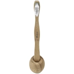 A bamboo toothbrush in natural tan colour, with soft bristles, resting in a round holder. It features a logo.