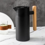 A drink bottle with a sleek black finish and a wooden handle, featuring a spout and a minimalist design.