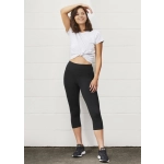 A model wears black 3/4 leggings paired with a white cropped T-shirt and sneakers, standing against a light wall.