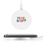 A round white wireless charger with a logo on top, positioned near a smartphone on a white surface.