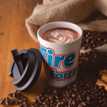 A reusable coffee cup in cream and blue with a black comfort lid, surrounded by coffee beans and cinnamon.