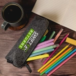 A grey felt utility case containing colorful pens and markers, alongside a mug and a notepad.
