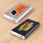 Two power banks displayed on a wooden surface: one silver with an orange label, and one black with a colorful logo.