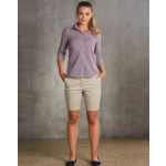 A model wearing khaki chino shorts paired with a button-up shirt, standing against a textured grey background.