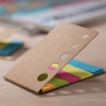 A set of coloured sticky notes in a cardboard holder, featuring pink, green, blue, and orange notes.