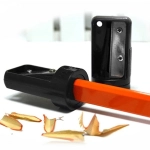 A carpenter pencil sharpener in black and orange, with wood shavings beside it. It features a logo on the casing.