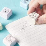 A set of pastel-coloured rubber erasers featuring cute animal designs, being used on lined paper.