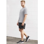 A man stands wearing grey sports shorts and a matching grey t-shirt, with black athletic shoes. The backdrop is white.