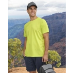 A man wearing a bright yellow short-sleeve performance T-shirt stands against a mountainous backdrop, holding a bag.