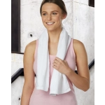 A white terry velour fitness towel, 110x30 cm, held by a smiling woman in a pink top, against a concrete backdrop.