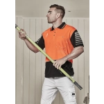 A man wearing an orange and black short sleeve polo shirt stands holding a green pole. The shirt has a logo.