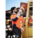 A man in an orange and navy long sleeve polo lifts a traffic cone near a yellow vehicle. The scene is outdoors.