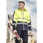 A man in a high-visibility yellow and navy softshell jacket holds red bolt cutters, set against a construction backdrop.