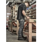 A man in black cargo pants and a black shirt standing at a workbench in a workshop, focused on a task.