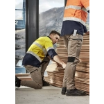 Two workers in high-visibility jackets and stretch cuffed pants, stacked wood planks in an industrial setting.