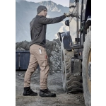A man wearing beige curved cargo pants and a long-sleeve shirt stands next to a truck in a rugged outdoor setting.