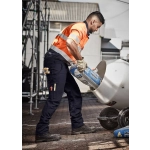 A man in orange and grey high-visibility workwear pours from a bag into a mixer, wearing navy rugged cargo pants.