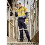 A worker in a yellow and navy work shirt and cargo pants, wearing gloves and a hard hat, on a metal staircase.